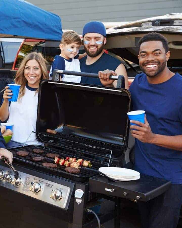people standing around a grill at a tailgate party at home smiling