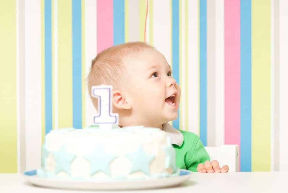 smiling baby in front of striped background with first birthday cake in front