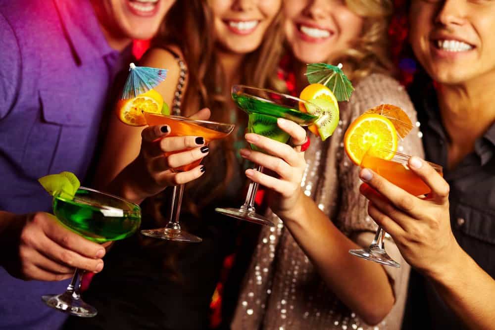 group of friends holding fun and colorful mixed drinks with fruit and umbrella picks in a party setting