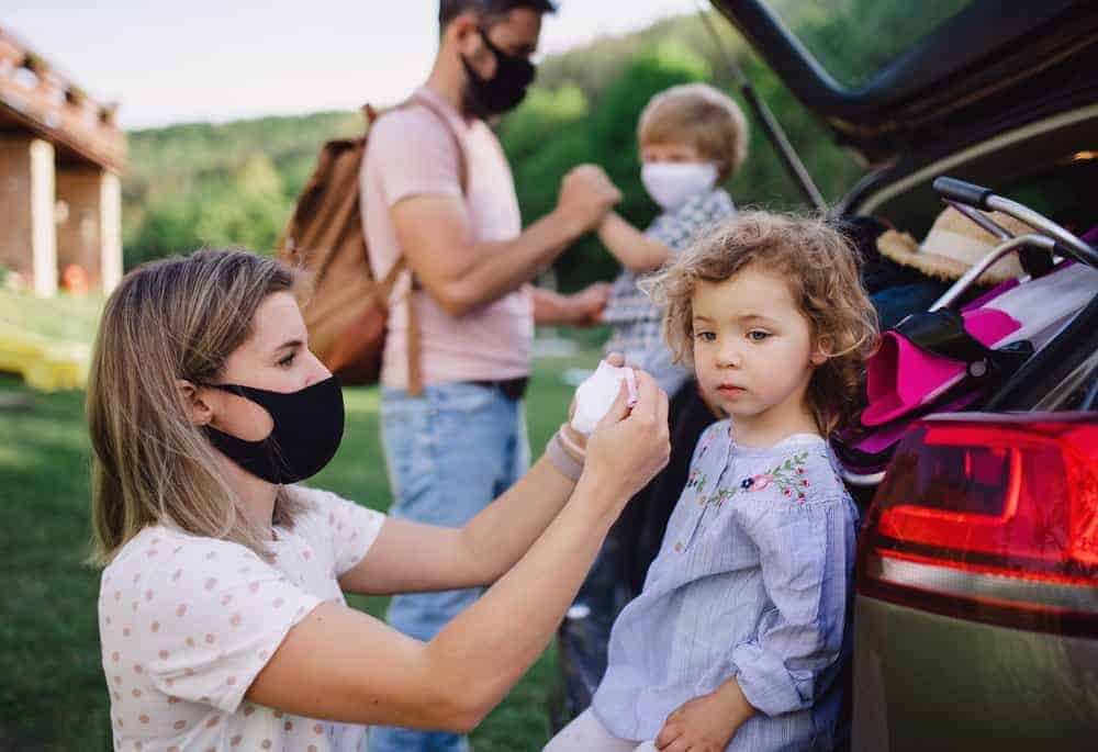 Happy family with two small children by car wearing face masks.