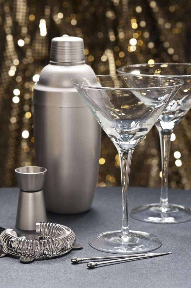 Two Martini glasses with bartender tools in front of gold glitter background