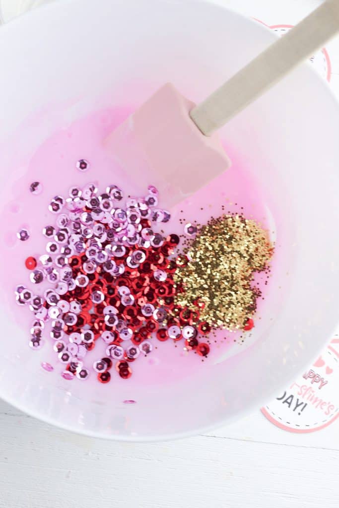 spoon mixing glitter and sequins with ingredients for valentine's day slime gift