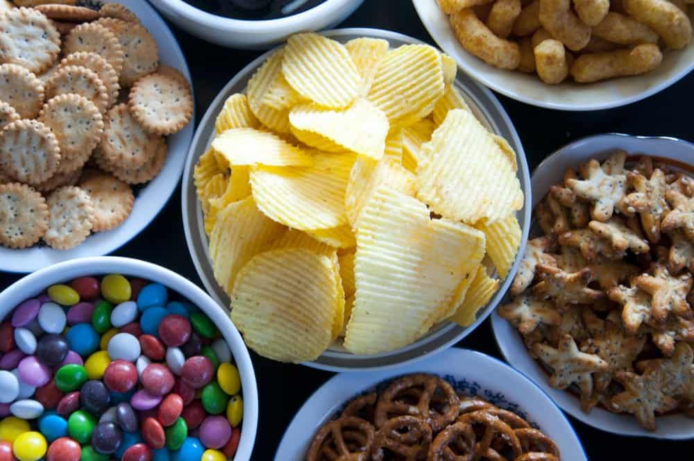 bowls of simple party snacks for kids birthday parties, including chips, crackers, candy, pretzels, and puffs