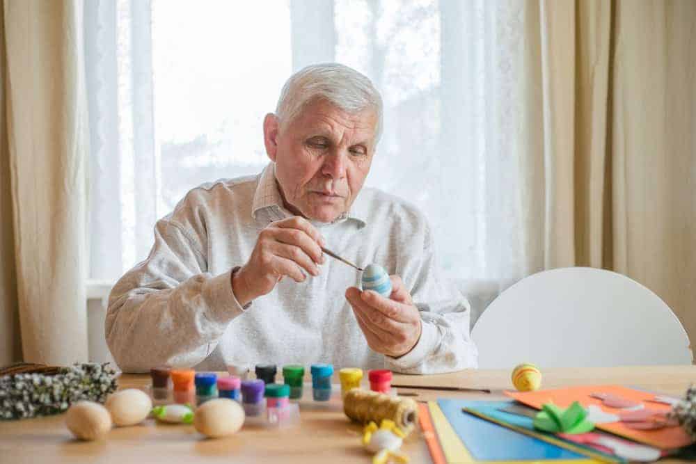 senior man painting wooden easter eggs