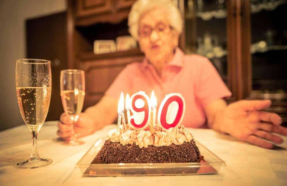 Grandmother sitting at table with birthday cake with candles that say 90 with champange glasses