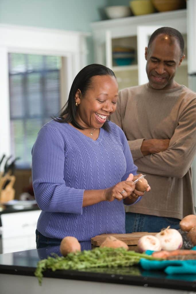 black senior woman cooking in home with male smiling behind her