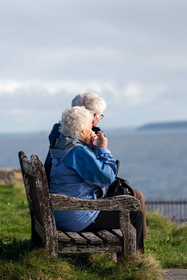 senior citizens sitting on bench overlooking ocean