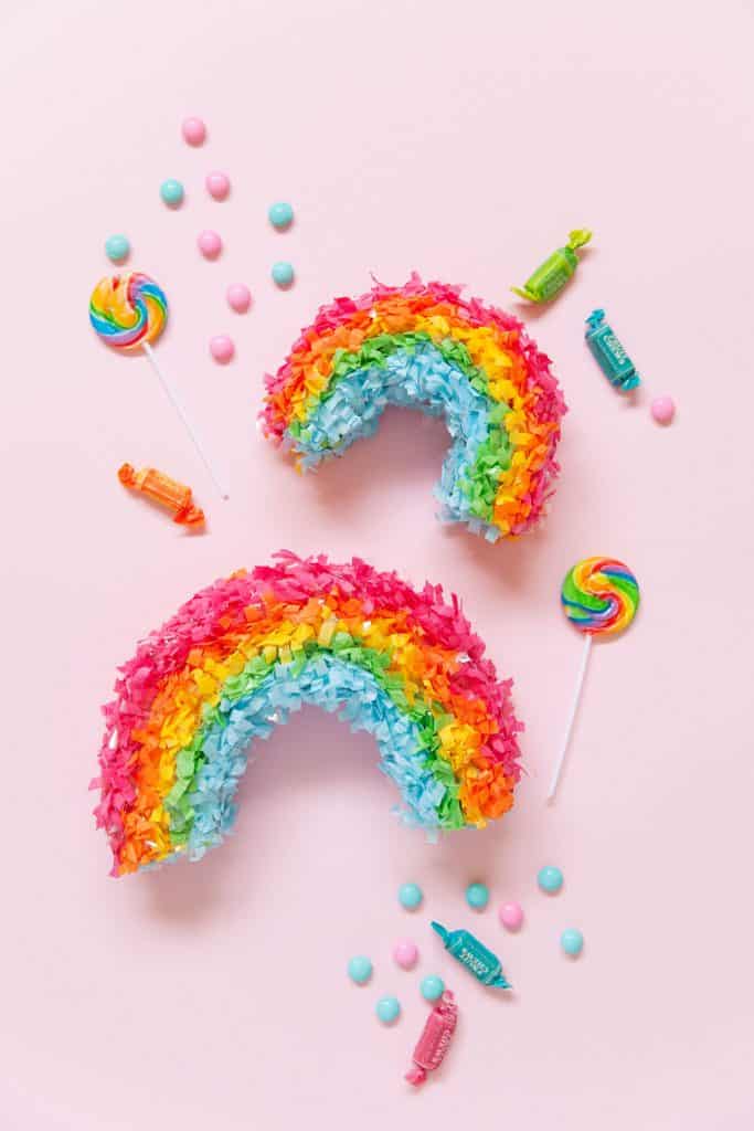 two mini rainbow pinatas with brightly colored candy on pink background