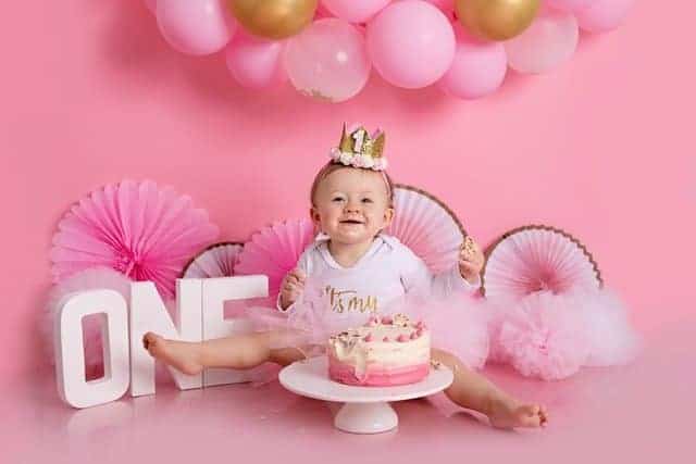 smiling baby with first birthday cake and pink decor