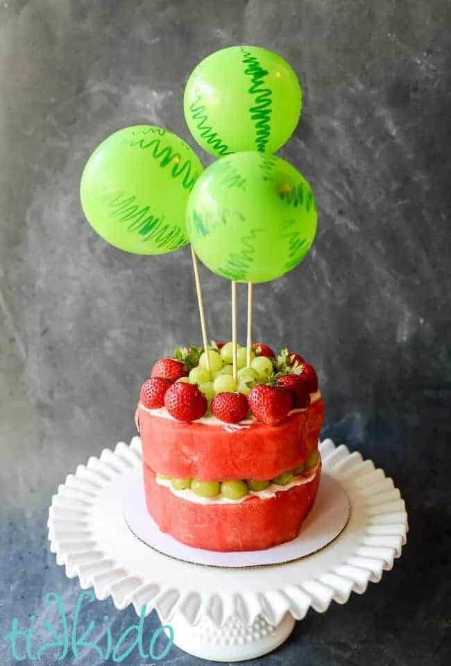 watermelon cake with balloon cake topper on a white cake stand