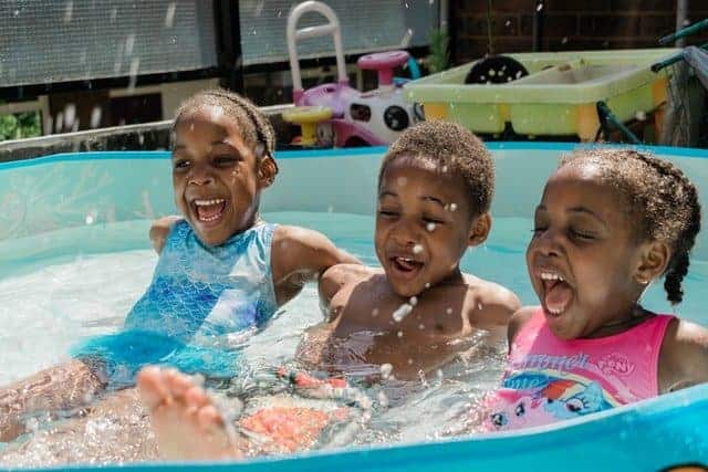 three children reclined in a kiddie pool kicking feet and laughing