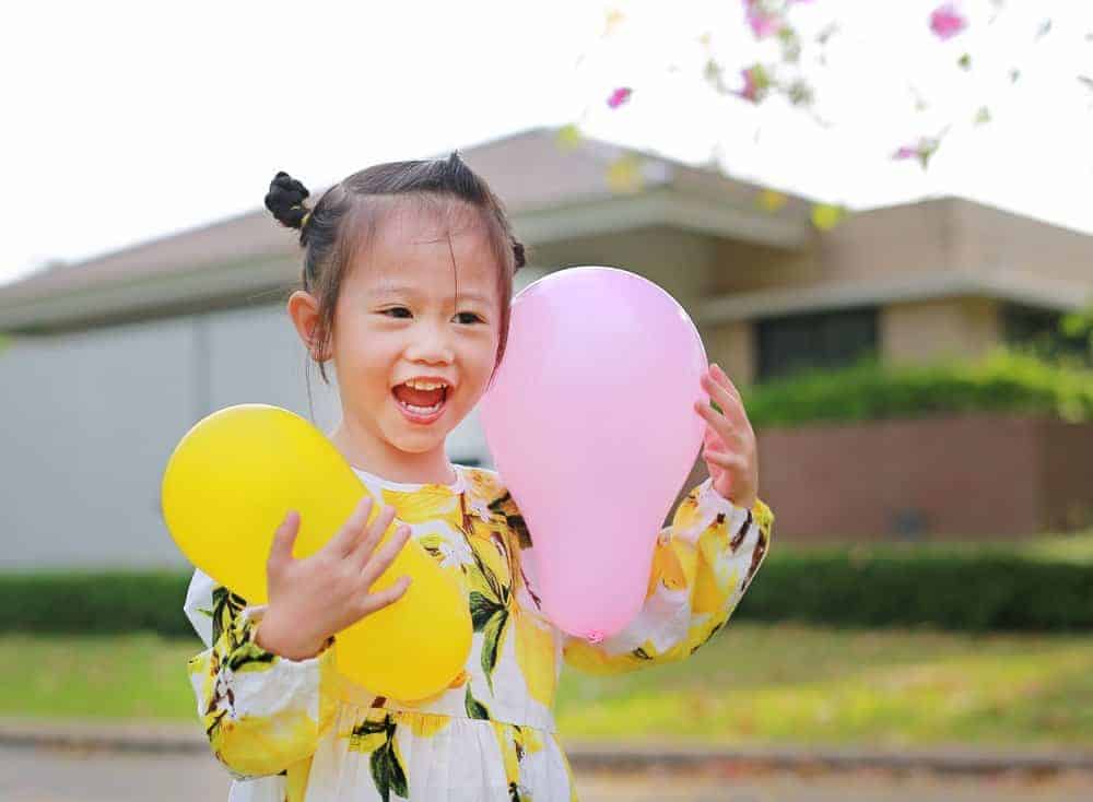 laughing girl holding two oval balloons