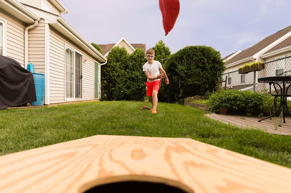 front row view of boy throwing a bean bag to a cornhole board