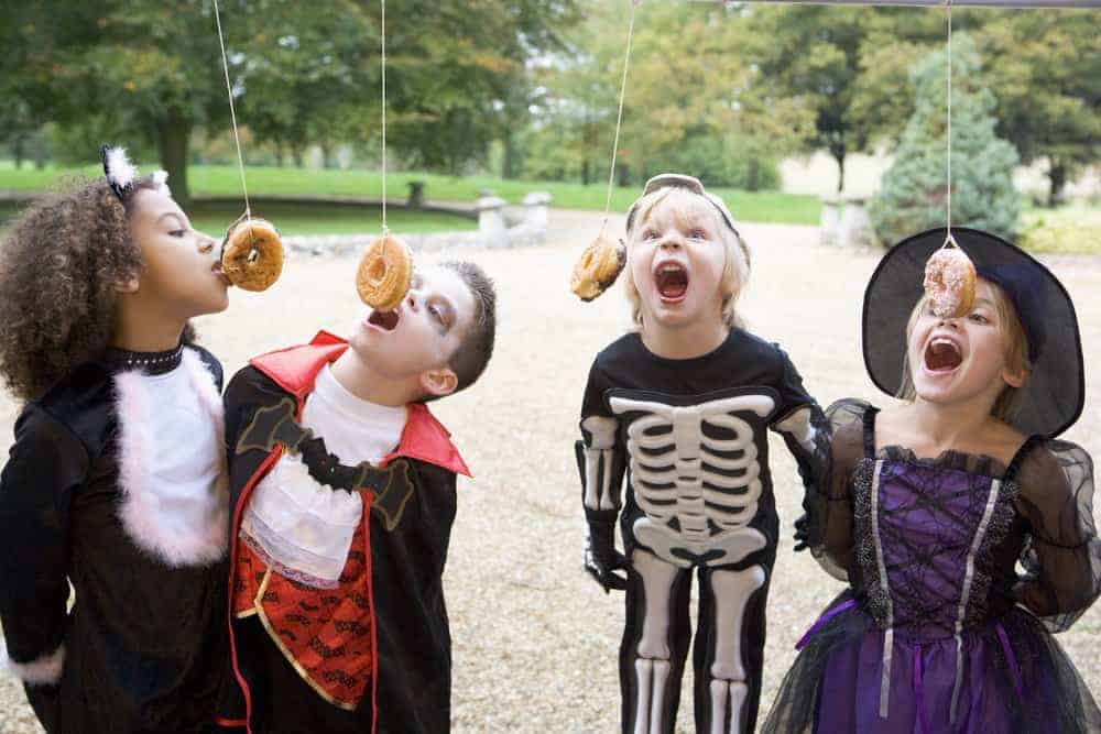 children wearing halloween costumes eating donuts hanging from a string