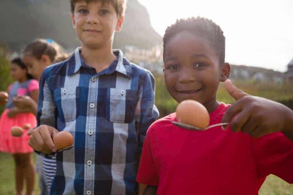 two boys smiling at camera while holding and egg on a spoon for relay race