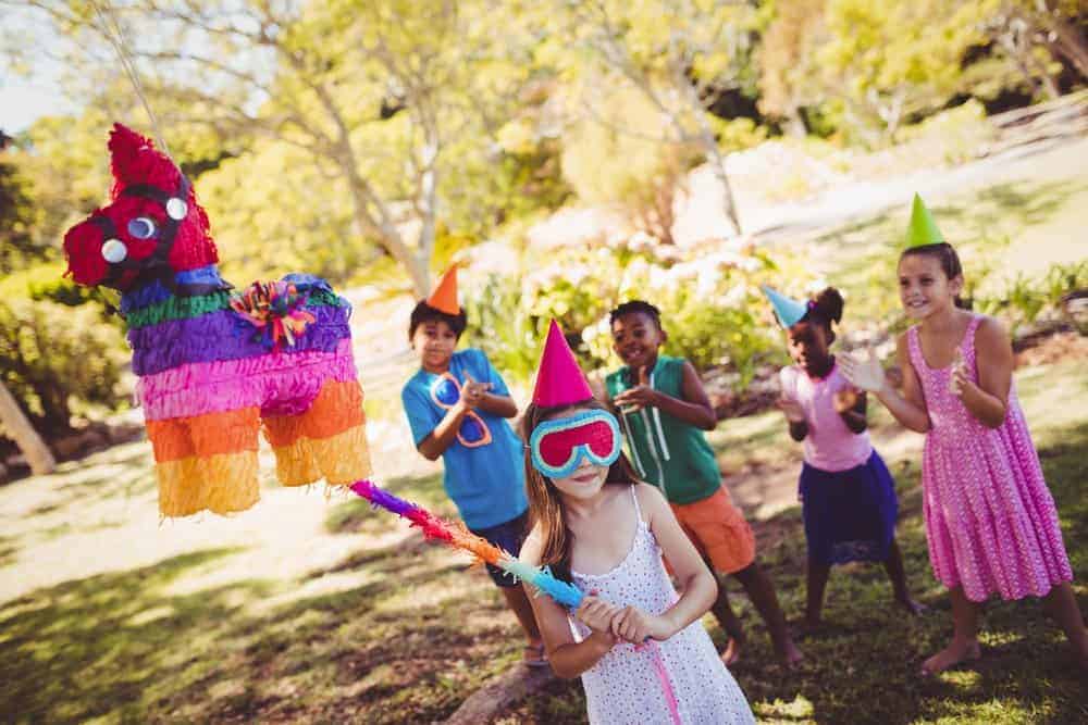 kids at a party cheering on a girl wearing a blindfold getting ready to hit a pinata