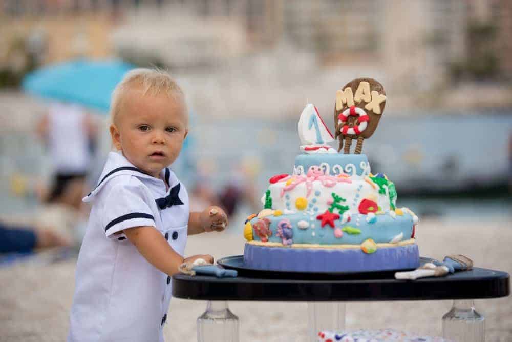 toddler baby standing next to a ocean themed birthday cake at a beach birthday party