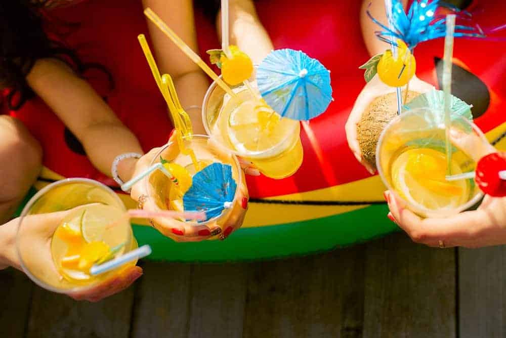 overhead shot of summer cocktails being held by hands with summer party decorations in cups