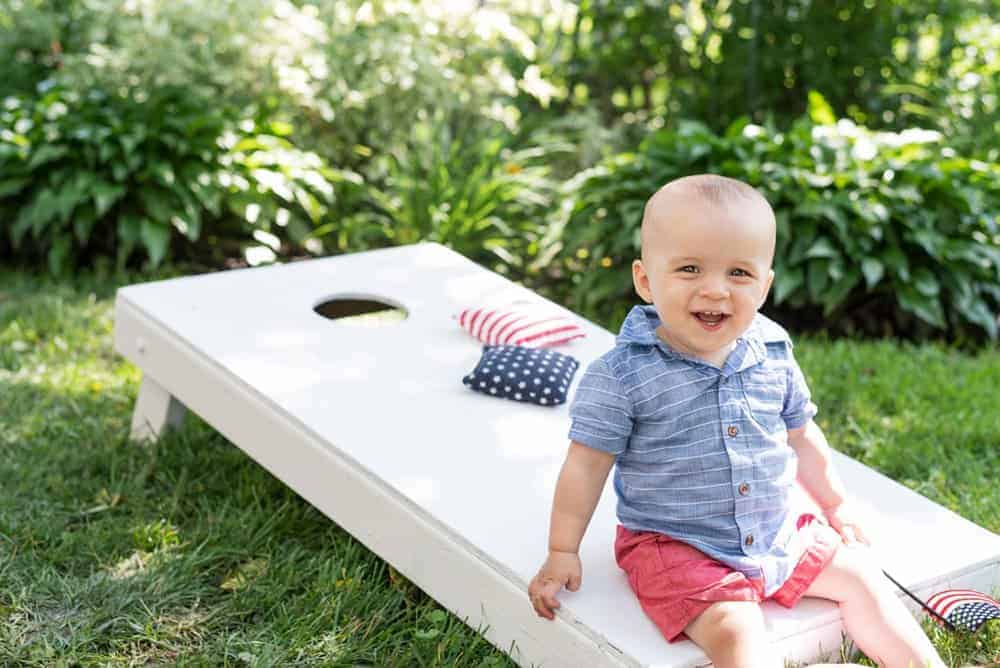 boy in patriotic colors sitting on a white corn hole aord with stars and stripes beanbags