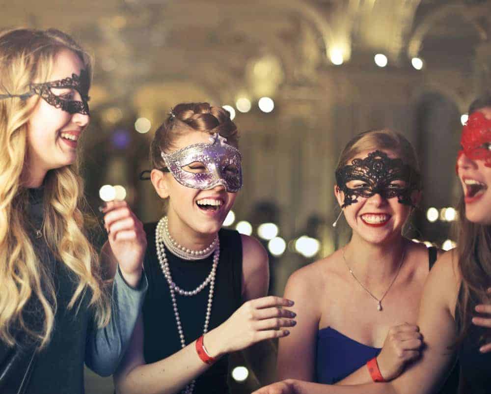 four women laughing and smiliing while wearing masquerade masks at a costume party