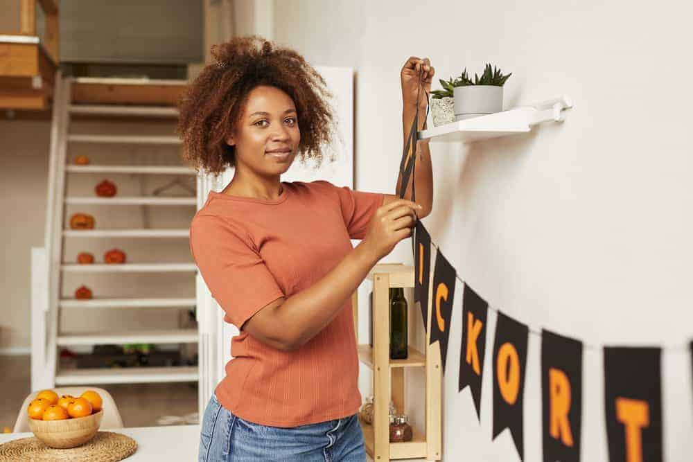 Attractive young African American woman decorating room with garland for Halloween party