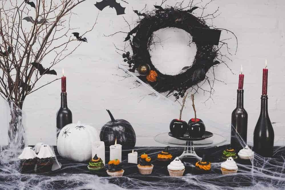 spooky office halloween decorations with modern flair including black and white pumpkins, red candles in wine bottles, and bats on branches with black wreath