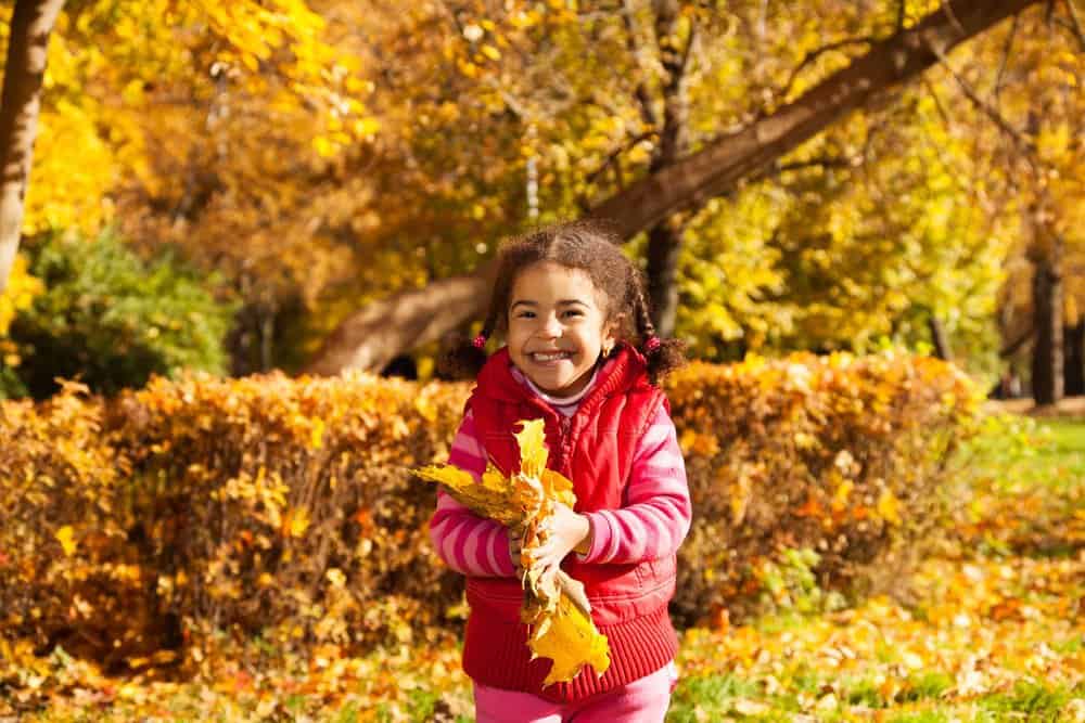 smiling girl playing outside in fall leaves