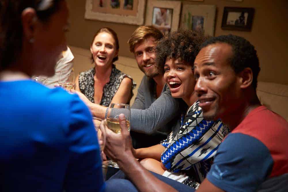 group of friends sitting at a house partyh holding wine and looking in amazement at person with back to camera view