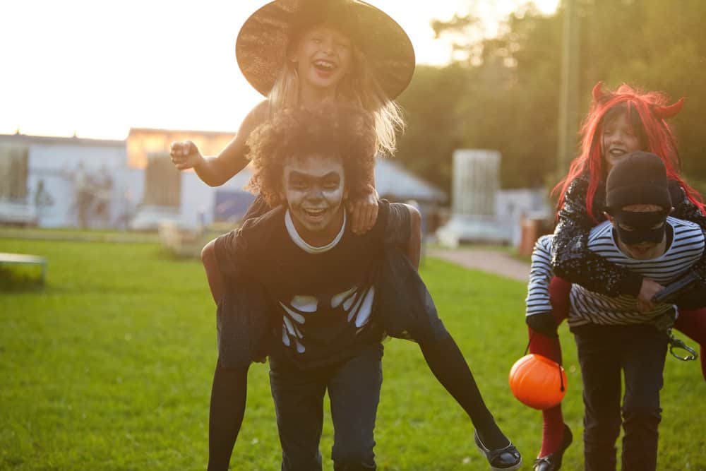 preteen kids wearing halloween costumes and playing an kids halloween party game by giving piggy back rides to friends in a relay