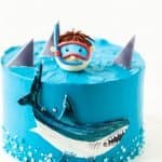 Sea and shark themed cake with blue cream cheese frosting on the white background. Diver in a mask. Snorkelling among the sharks. Funny birthday cake. Danger in the sea. Homemade pastry