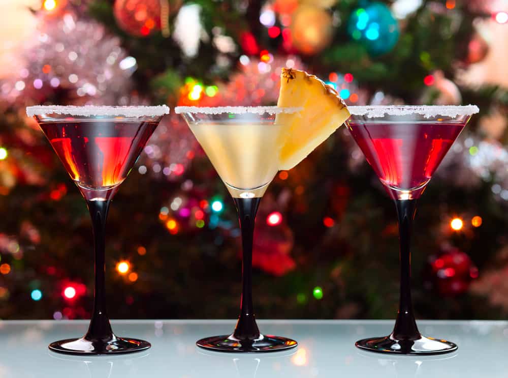 three martini glasses with different drinks in front of a decorated christmas tree giving off a christmas cocktail party vibe