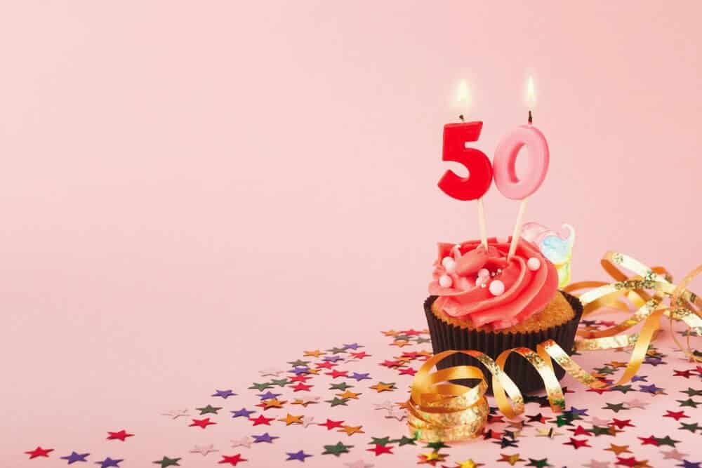 pink cupcake with number candles 50 on a pink background with confetti