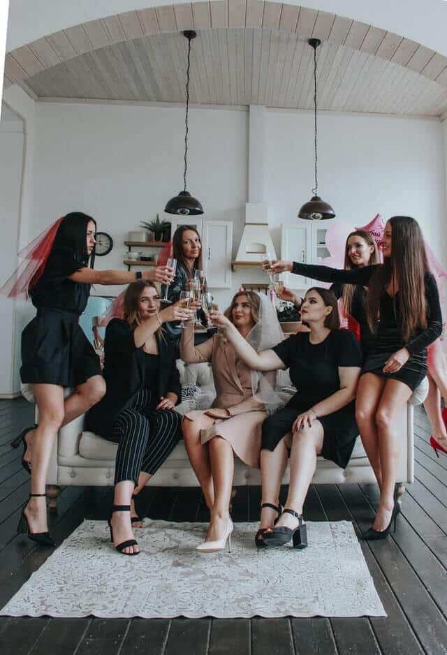 group of women toasting glasses at a bachelorette party with the bride wearing a white veil and the bridesmaids wearing pink veils