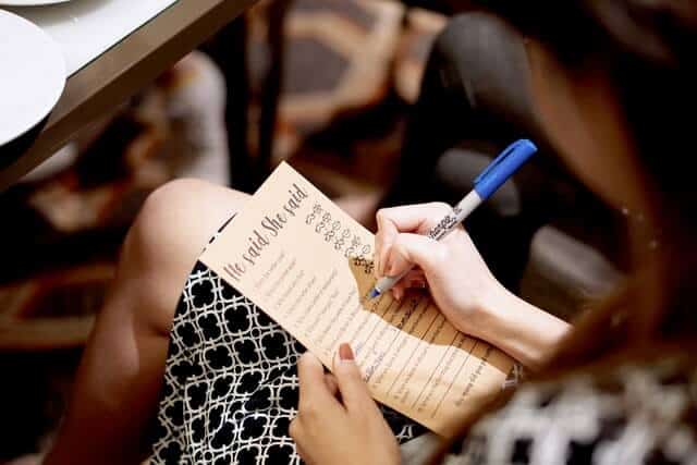 woman sitting with her legs crossed writing on a printable bridal shower game paper