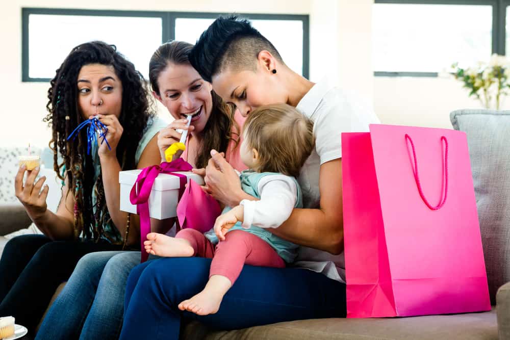 group of three women sitting on couch with a 1 year old celebrating the baby's first birthday with presents and noisemakers