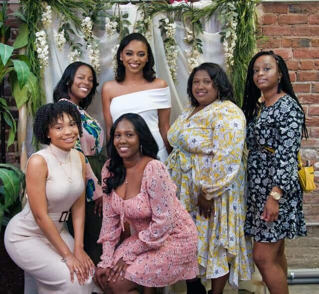 group of women posing with a bride to be at her bridal shower in front of a floral backdrop