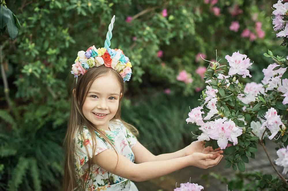 smiling girl wearing a floral unicorn party headband and touching a flowering tree