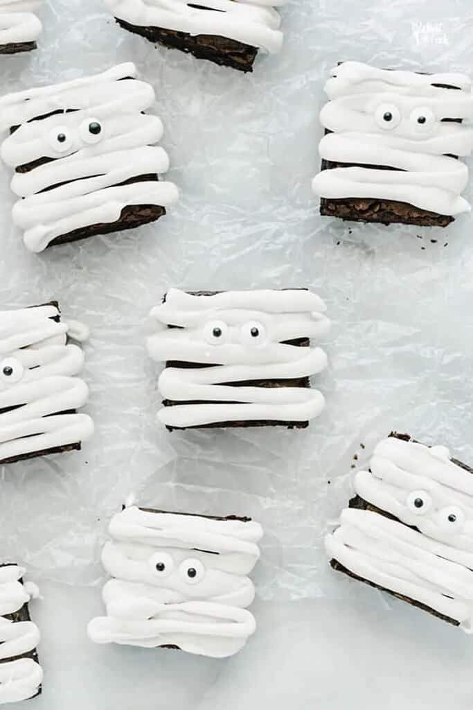 brownies laying on a white surface with frosting laying in stripes like a mummy with eyes