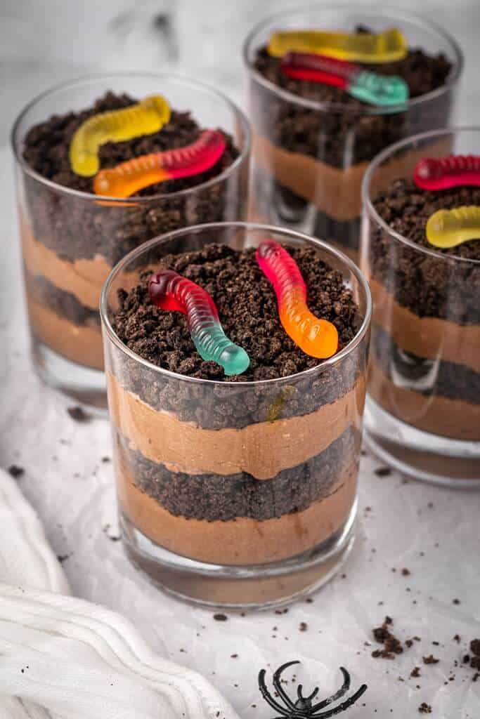 individual halloween pudding cups called graveyard dirt cups with layered pudding and crushed cookies and gummy worms