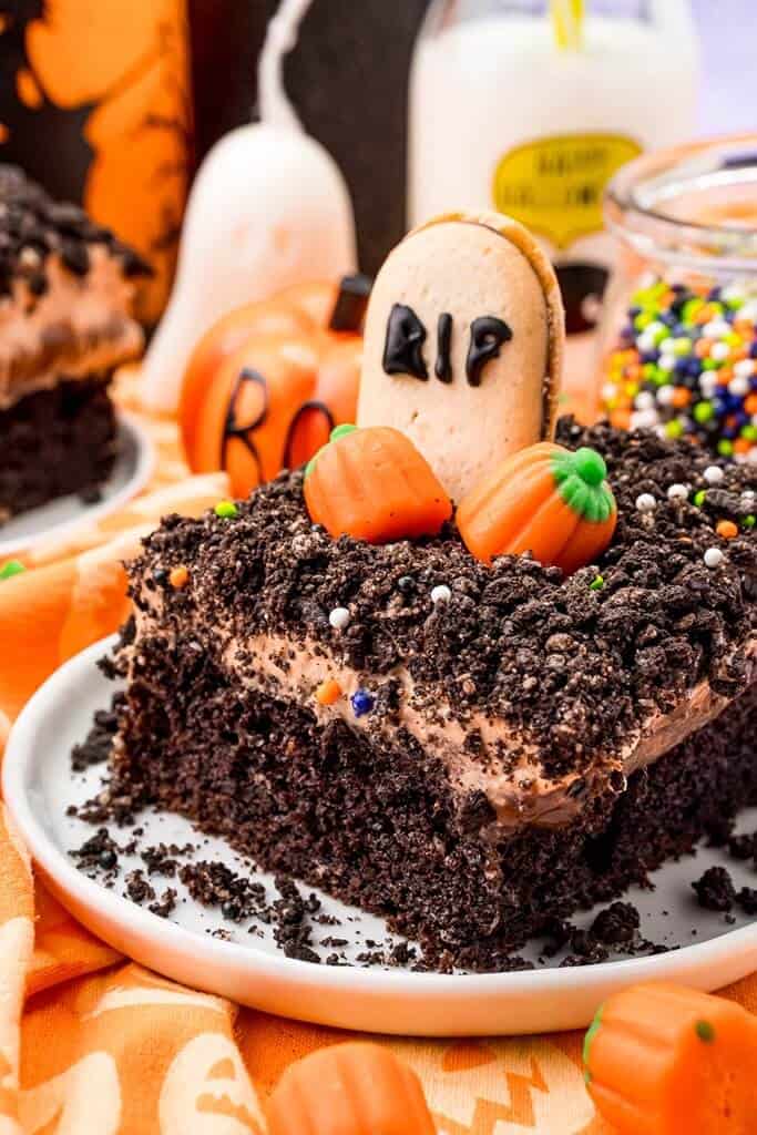 closeup of halloween dessert called graveyard dirt cake, consisting of layers of chocolate cake, frosting and crumbled cookies with a RIP cookie and pumpkins on top