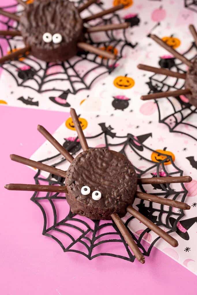 cute mini spider cakes with pretzel legs and candy eyes on a pink background