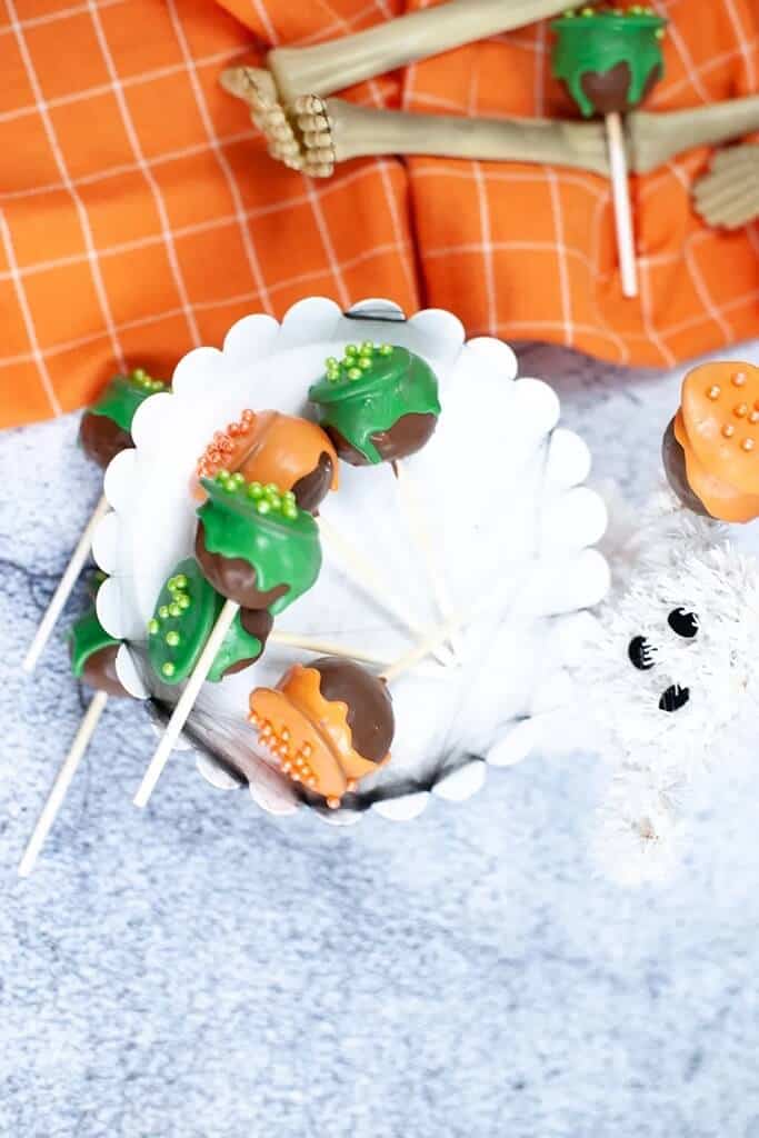 cake pops decorated like halloween cauldrons on a white tiered plate