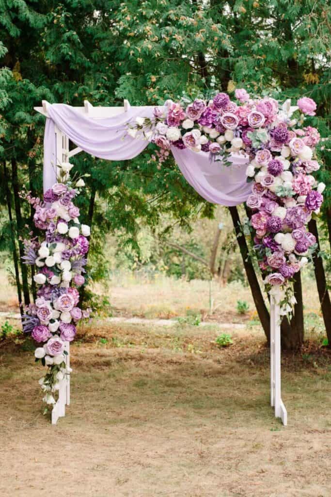 light purple fabric draped over a white wedding arch arbor with purple and white wedding flowers