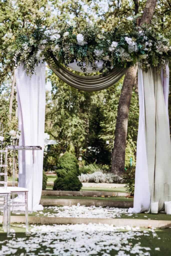 elegant wedding arch with draping fabric, white flowers and greenery in an outdoor wedding ceremony