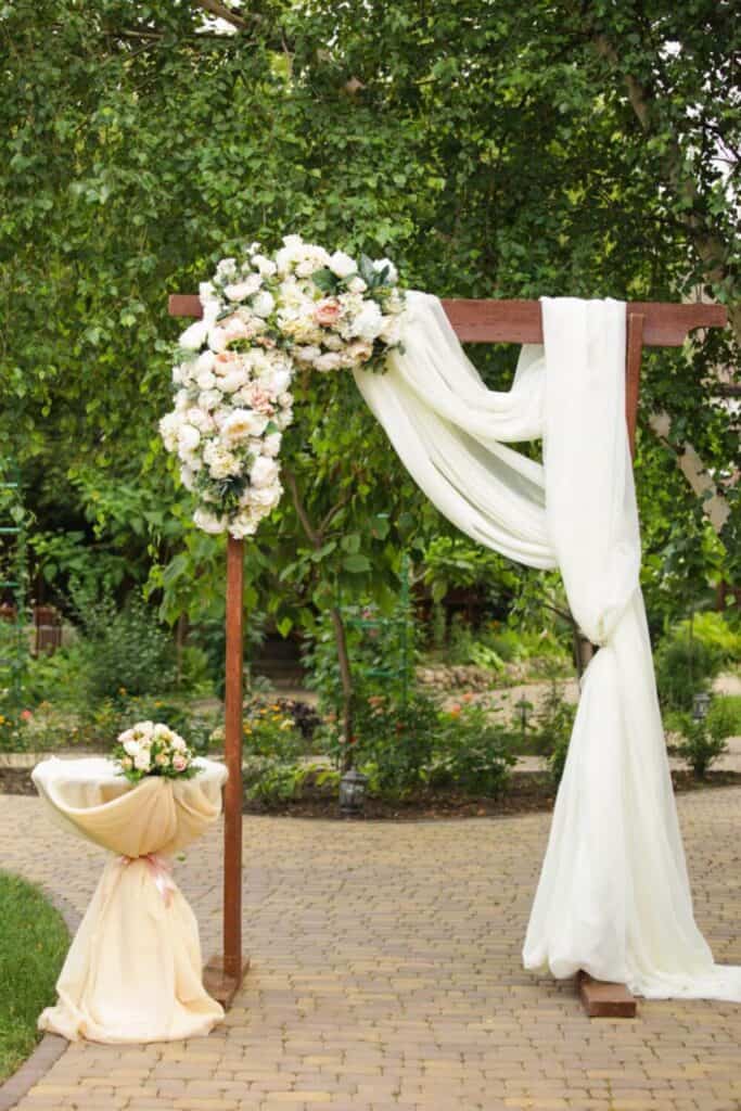 classic rustic wedding arch with white fabric draped over the top and edge with white flowers