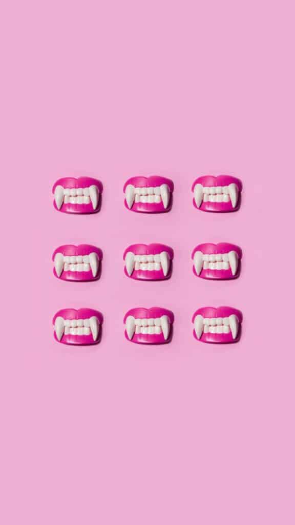 halloween wallpaper background image consisting of costume vampire teeth in a 3 by 3 grid on pink background
