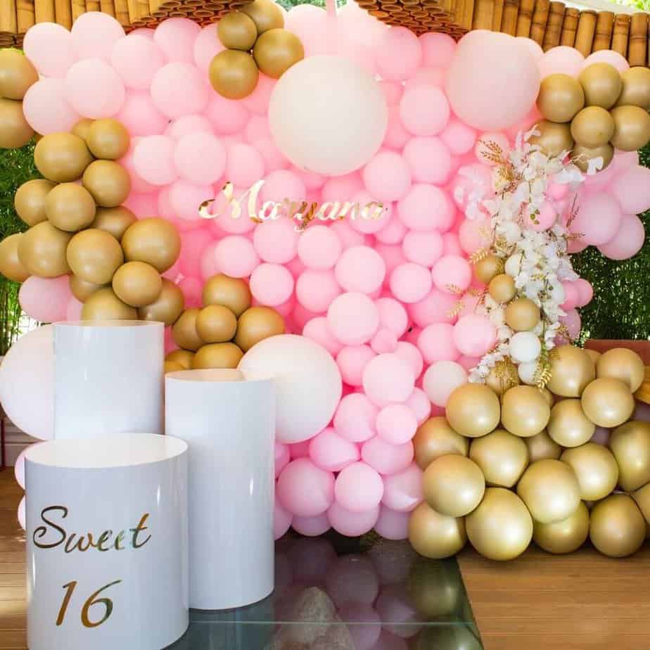 pink and gold balloon wall with three round white pillars that say sweet 16