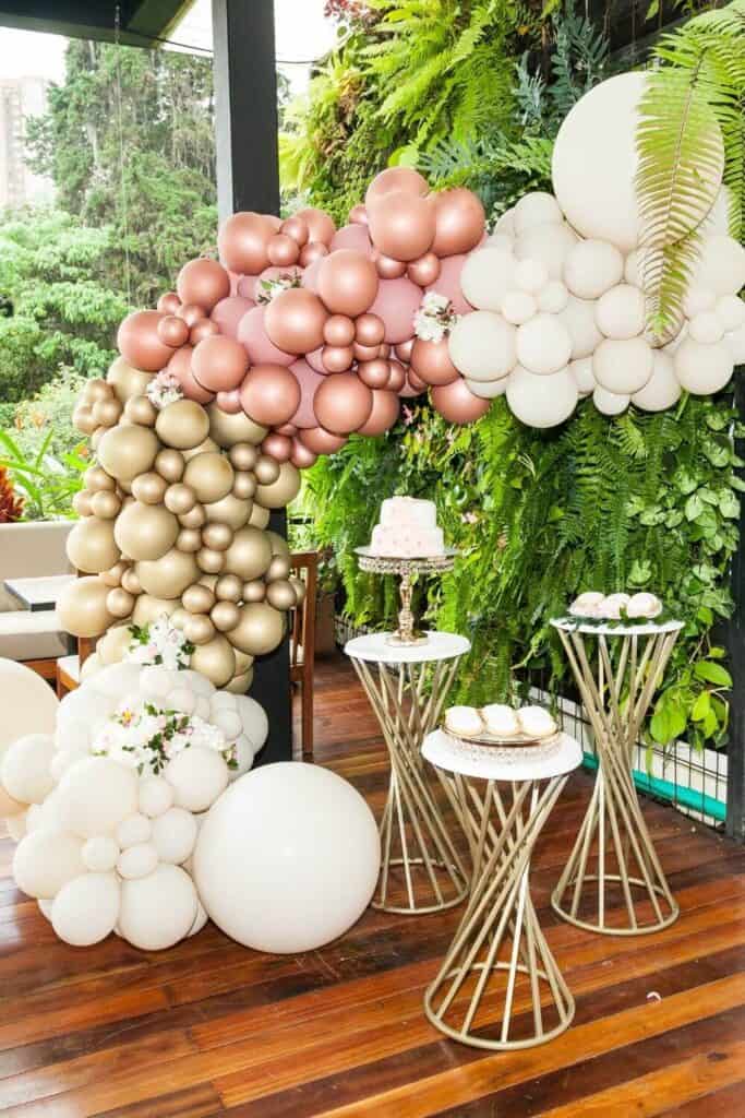 pretty pink, white and gold balloon arch in front of a greenery backdrop with gold treat tables