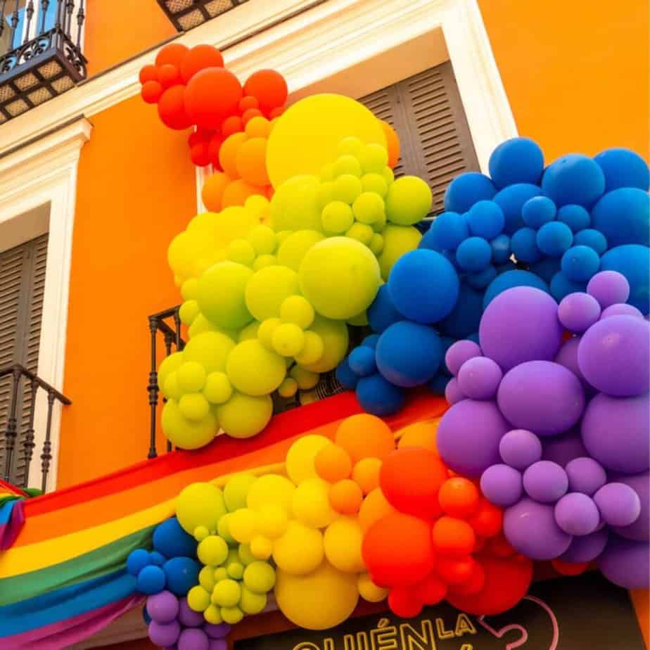 pride rainbow balloon clusters hanging on a building with a pride flag