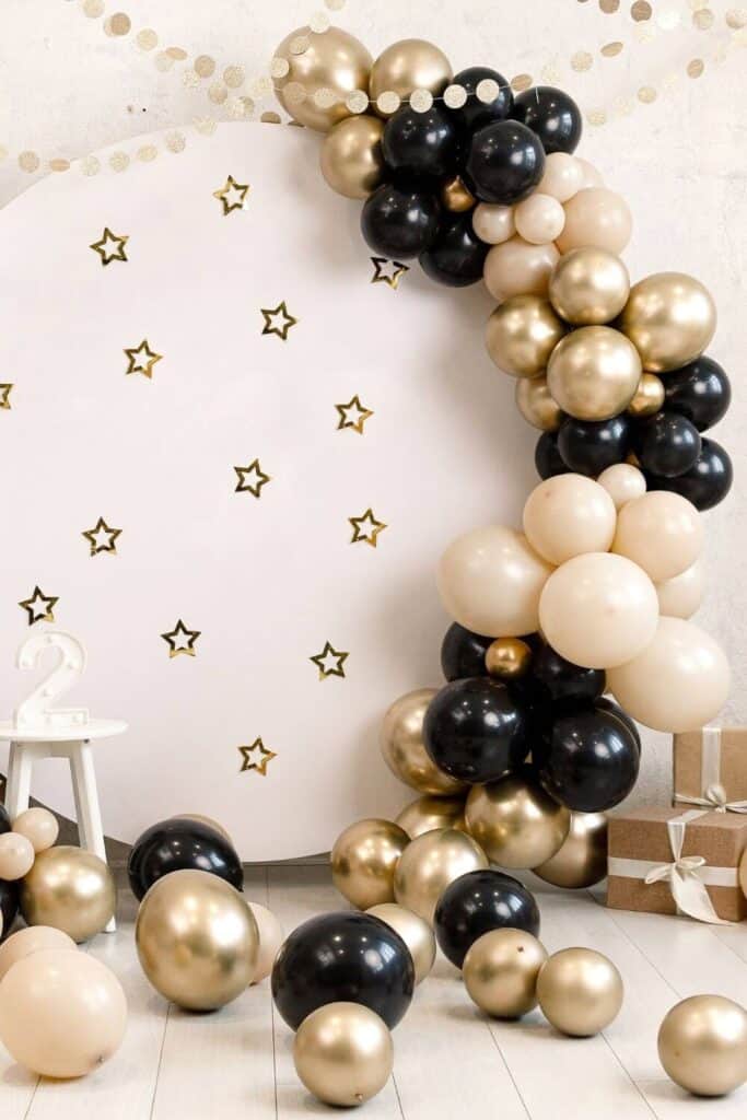 black, gold and tan balloon arch on a round backdrop